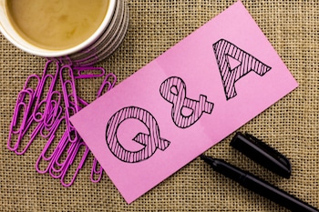 The letters "Q&A" on a pink slip of paper. Paperclips, a pen and a cup of coffee can be seen.