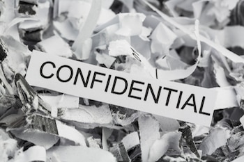 shredded paper, one piece of paper is still intact and it reads "confidential"