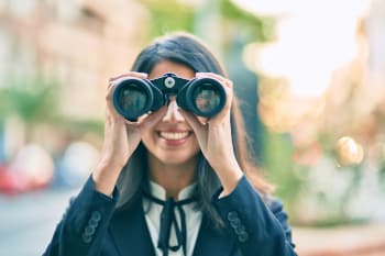 A person looking through binoculars toward the camera.
