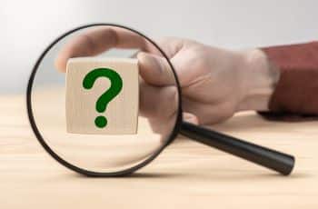 Magnifying glass with question mark in focus on wooden cube.
