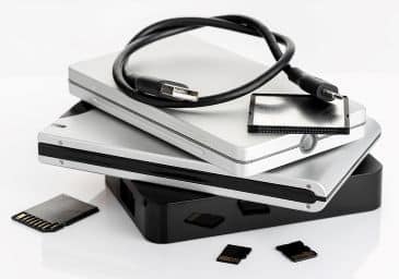 A pile of external hard drives and memory cards on white table