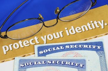 Two social security cards are laying on a table along with a pair of glasses and a document reading "protect your identity."