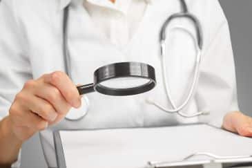 Medical professional looking through a magnifying glass at a document on a clipboard